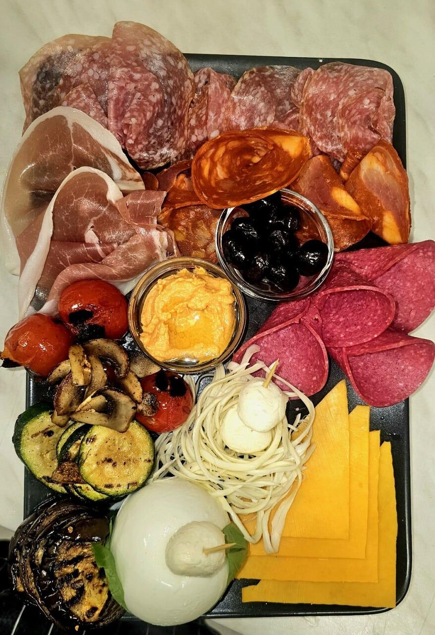 Reichhaltige Frühstücksplatte mit Salami, Parmaschinken, Käse, Oliven, Hummus und gegrilltem Gemüse